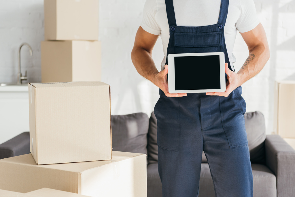 cropped view of mover in uniform holding digital tablet with blank screen near boxes in apartment  - Photo, Image