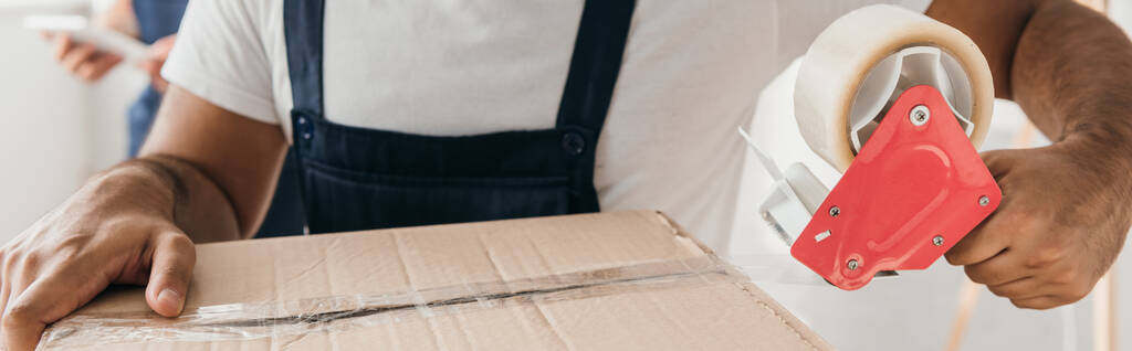 vista parziale di uomo in possesso di scotch nastro mentre scatola di imballaggio  - Foto, immagini