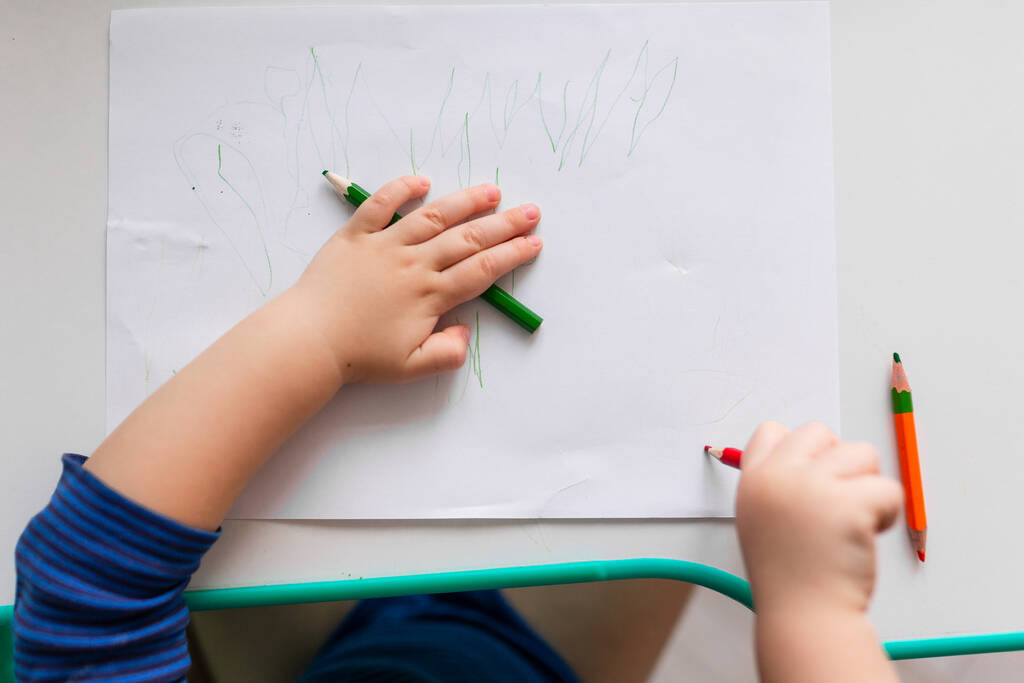 A kisfiú rajzol egy képet színes ceruzákkal, a kezekre koncentrál - Fotó, kép