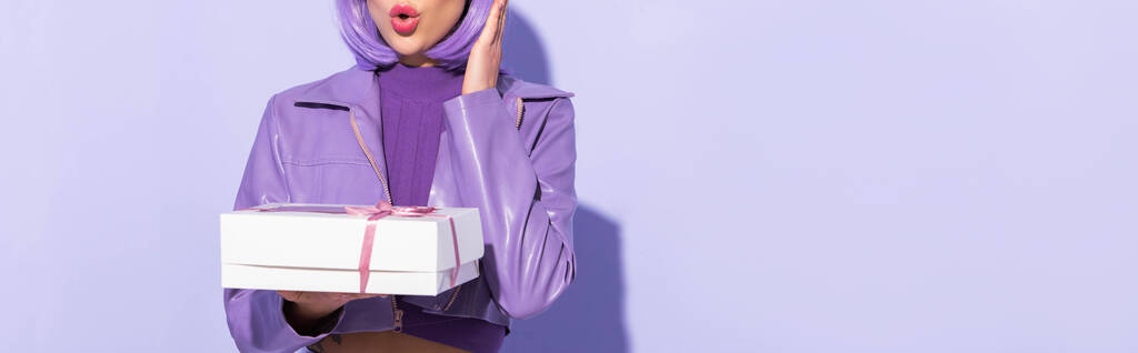 oříznutý pohled na šokované mladé ženy oblečené v panenském stylu s cupcake box na fialové barevné pozadí, banner - Fotografie, Obrázek