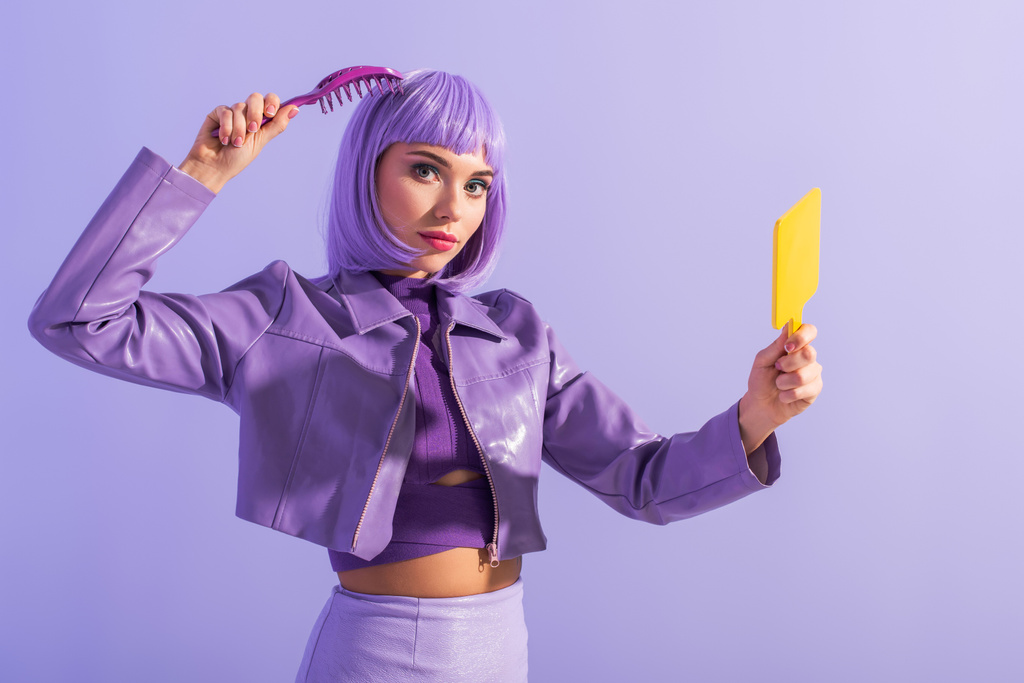 giovane donna vestita in stile bambola con spazzola per capelli e specchio su sfondo colorato viola - Foto, immagini