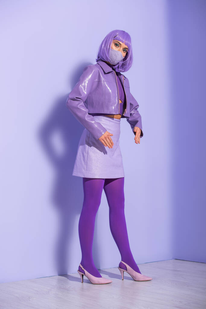 jeune femme habillée de style poupée en masque médical sur fond violet coloré - Photo, image