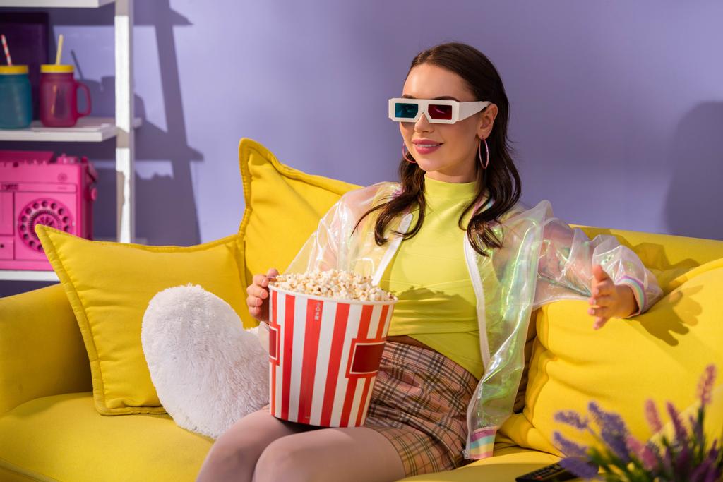 smiling young woman posing as doll with popcorn in 3d glasses on yellow couch - Photo, Image