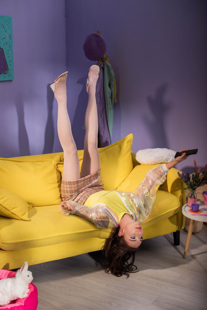 遠隔操作で黄色いソファの上で人形のふりをする若い女性 - 写真・画像