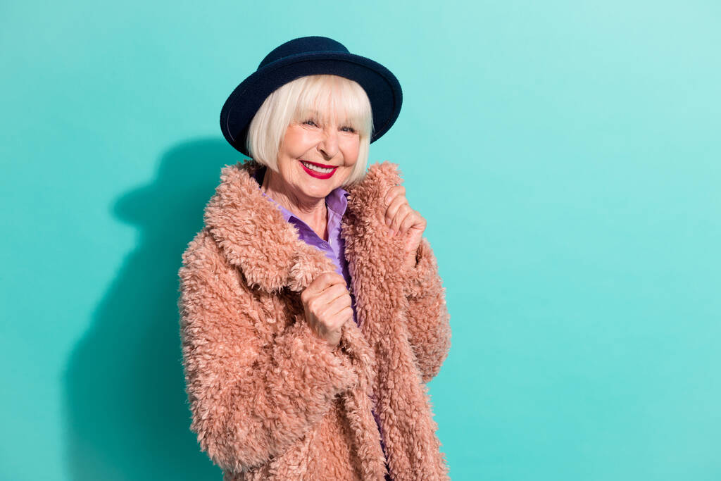 Foto de dulce mujer bastante vieja vestida de abrigo vintage gorra sonriente aislado color turquesa fondo - Foto, Imagen