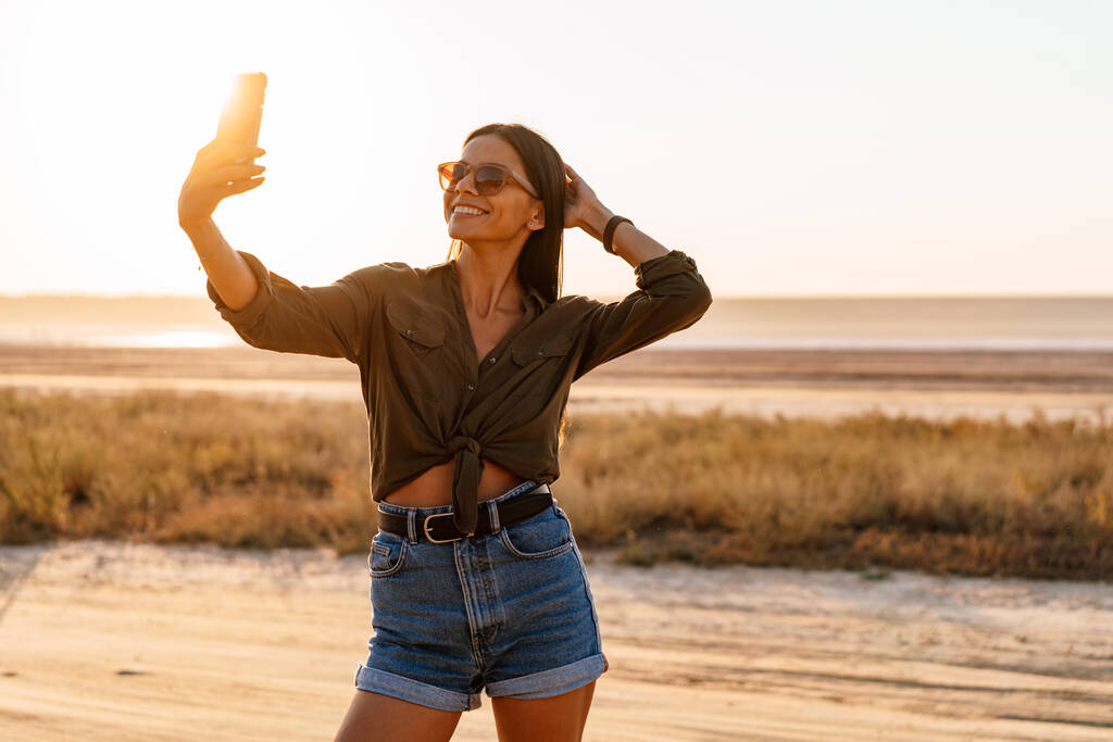 Kaunis iloinen tyttö ottaa selfie matkapuhelimeen kävellessään luonnossa kesällä - Valokuva, kuva