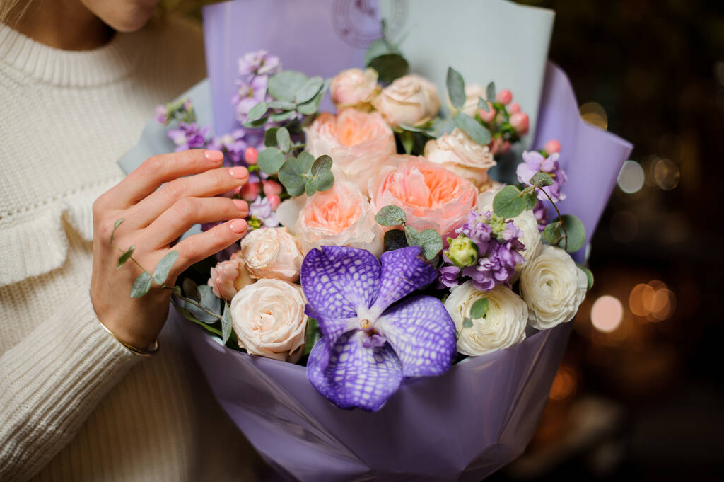 Nahaufnahme eines niedlichen Straußes frischer Blumen in lila Papier gewickelt in weiblichen Händen - Foto, Bild