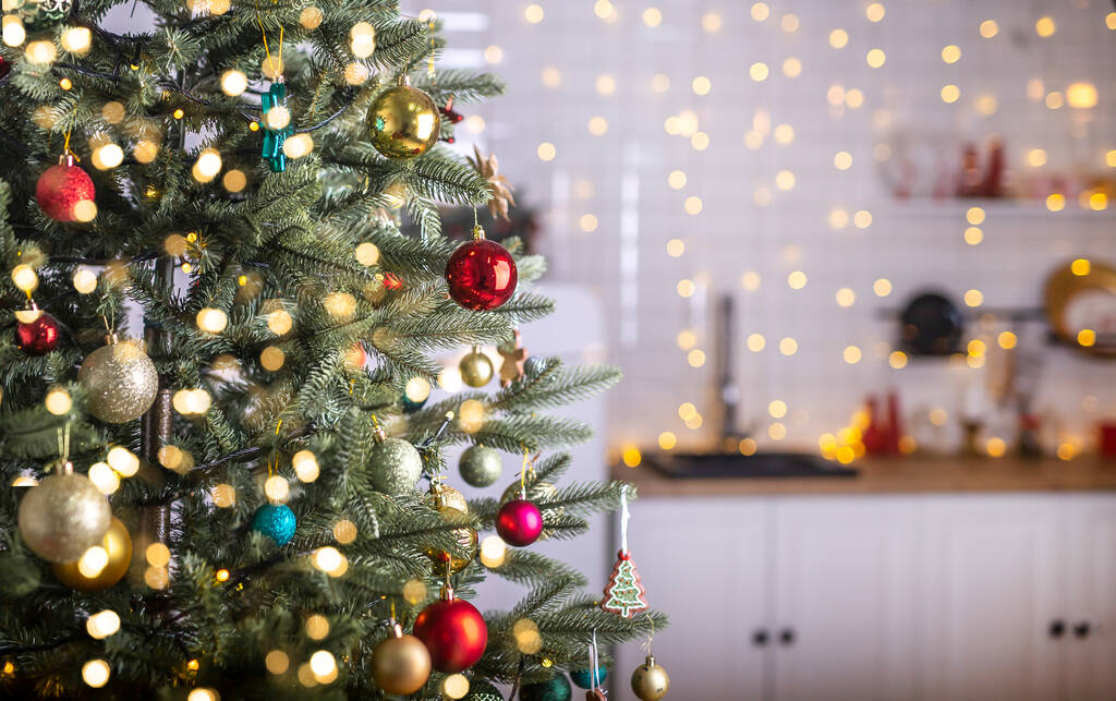 Festive fir tree branches with shiny red and golden baubles, balls, xmas ornaments and bright warm lights, garland. kitchen interior on blurred background. - 写真・画像
