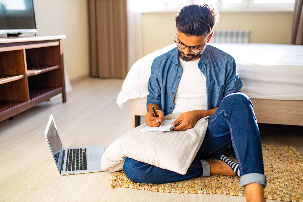 indyjski brodaty mężczyzna siedzi na podłodze i dokonywania obliczeń finansowych biznesu online w nowym mieszkaniu. - Zdjęcie, obraz