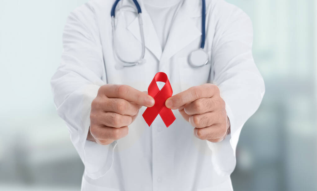 Doktor drží červenou stuhu vědomí na rozmazaném pozadí, detailní záběr. Světový den AIDS - Fotografie, Obrázek
