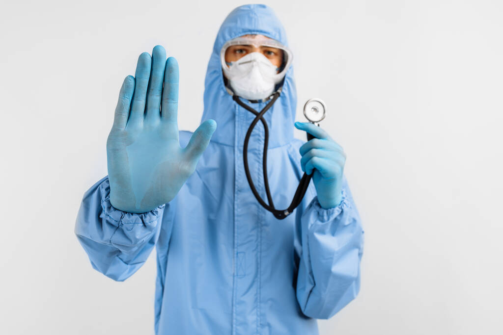 Doktor v ochranném obleku, masce, brýlích a rukavicích drží stetoskop, něco poslouchá, Medicína a koncept zdravotní péče - Fotografie, Obrázek
