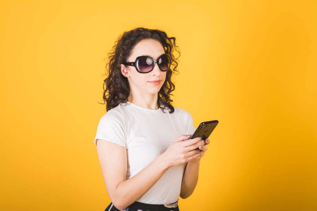 кучерява жінка використовує смартфон на жовтому фоні
 - Фото, зображення