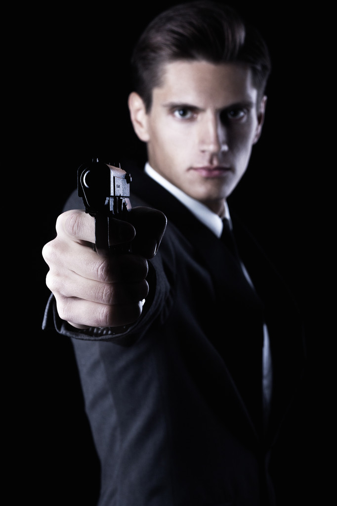 Young attractive macho in suit with gun on black background - Photo, Image