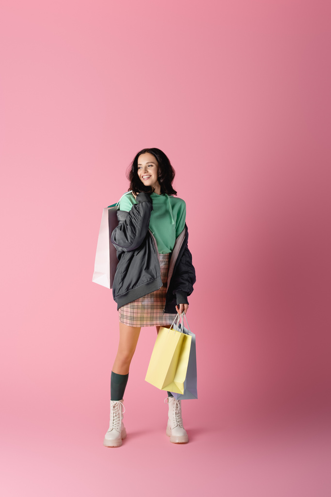 happy brunette young woman in casual winter outfit with shopping bags on pink background - Photo, Image