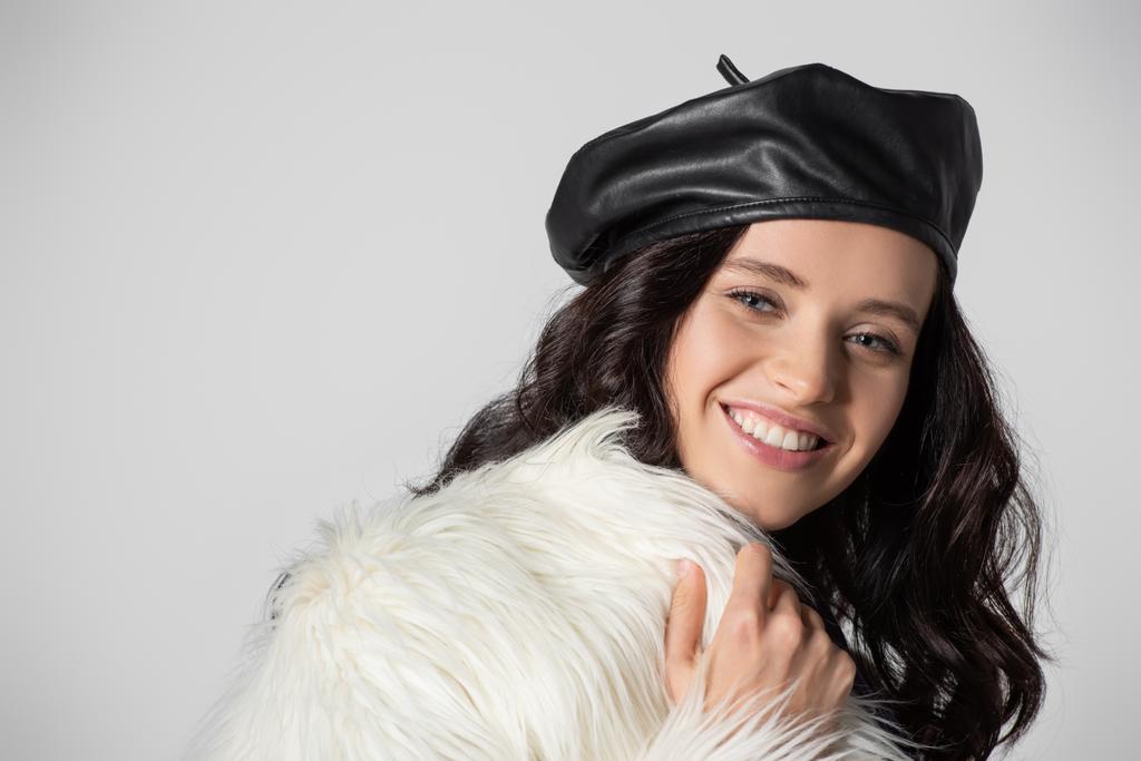 mosolygós barna fiatal nő elegáns fehér faux szőrme kabát és bőr svájci pózol szürke háttér - Fotó, kép