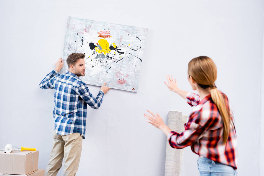 joven mirando a la mujer haciendo gestos cerca de la imagen en casa en primer plano borroso - Foto, imagen