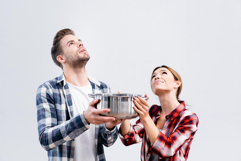 pareja joven mirando hacia arriba mientras sostiene la olla bajo el techo con fugas  - Foto, imagen