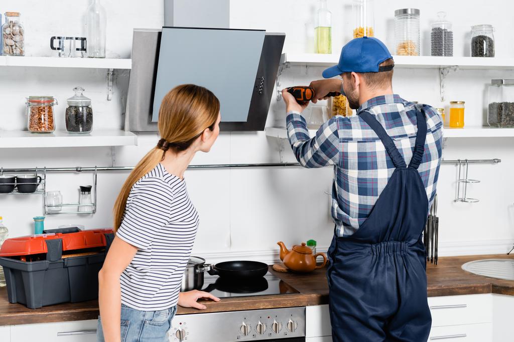 вид ззаду майстра з дрилем ремонту полиць біля жінки на кухні
 - Фото, зображення