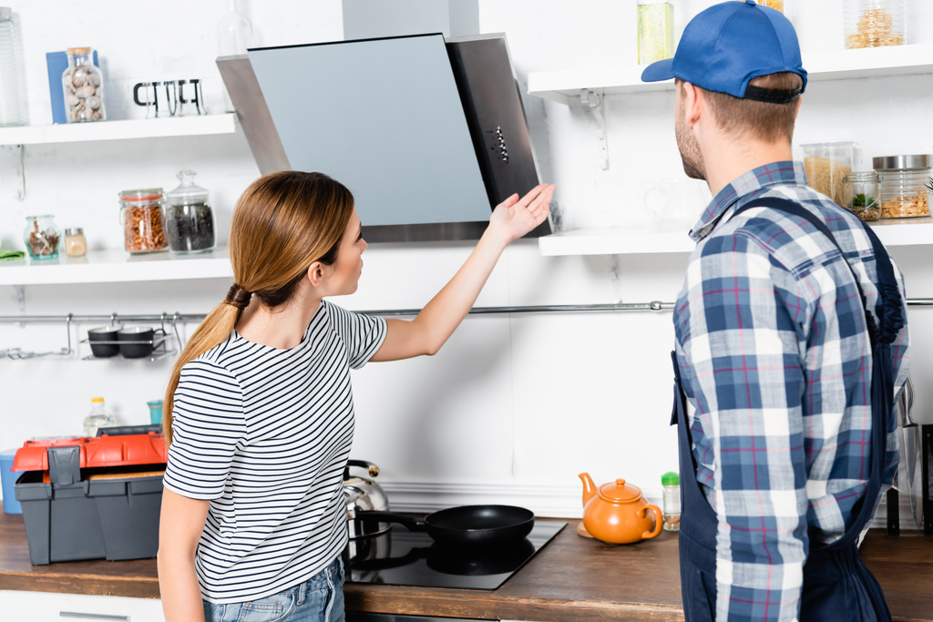 mujer joven señalando con la mano en los estantes cerca de manitas en la cocina - Foto, Imagen