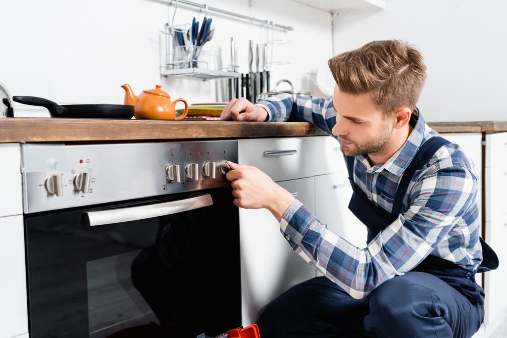 jonge klusjesman draaien oven knop in keuken - Foto, afbeelding