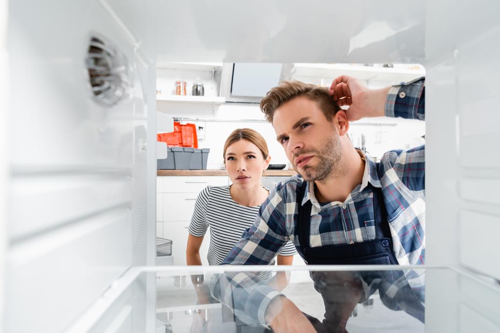 manitas reflexivo y mujer joven mirando congelador en primer plano borroso en la cocina - Foto, imagen