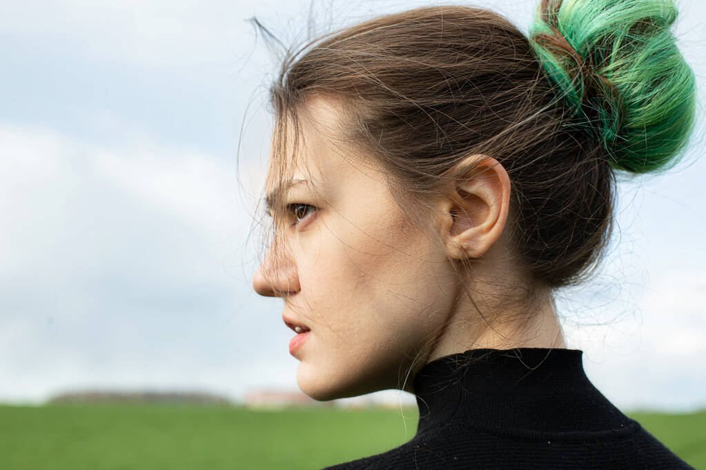 Emotioneel portret van meisje in zwart op groen veld met de hemel achter - Foto, afbeelding