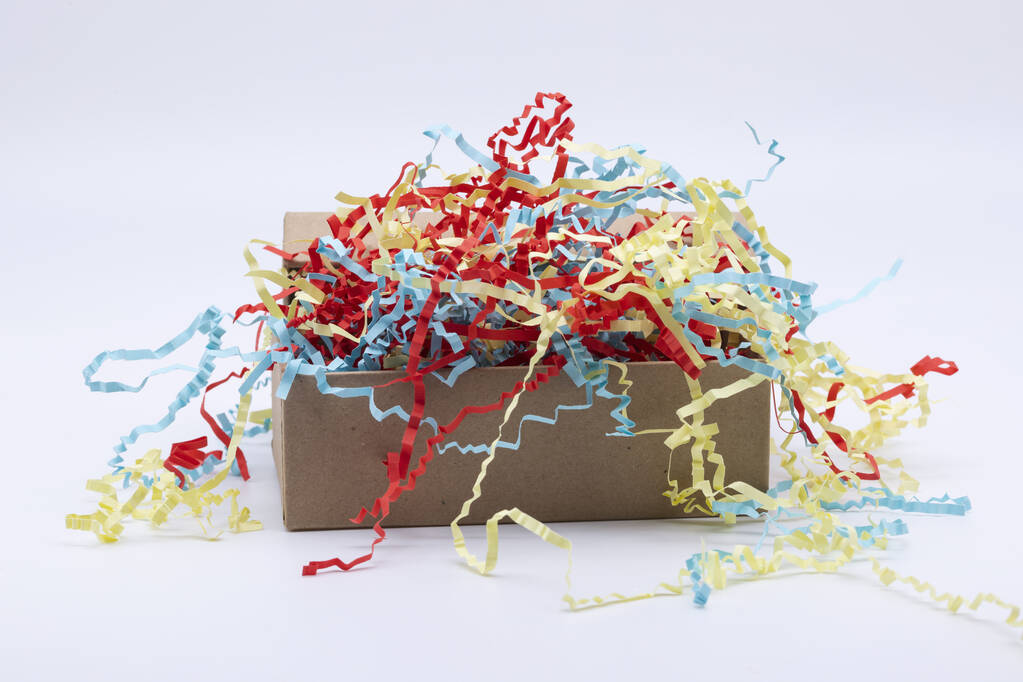 Open kartonnen doos gevuld met verstrengelde kleurrijke papieren strips verpakkingsmateriaal geïsoleerd op wit - Foto, afbeelding
