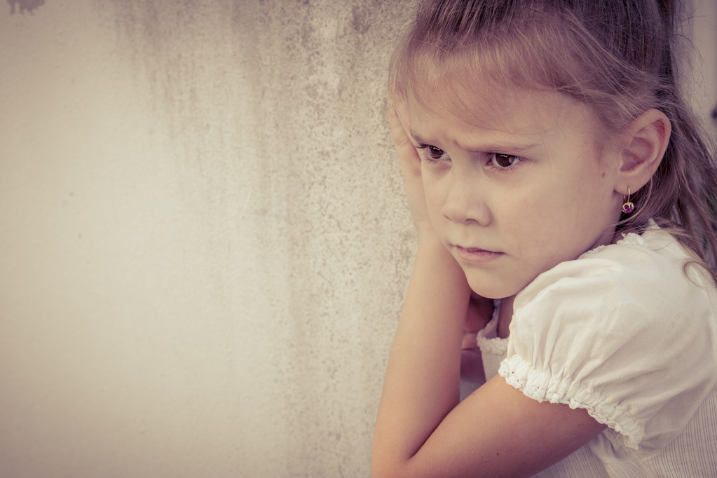 Portrait of sad little girl sitting near  wall in the day time - Photo, Image