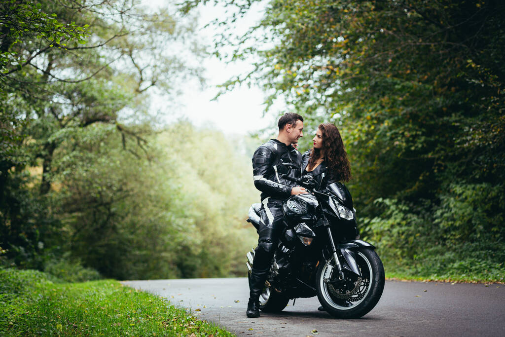 黒いスポーツバイクの近くの若いカップル男と女の子黒い革の服で森の中の道路上 - 写真・画像