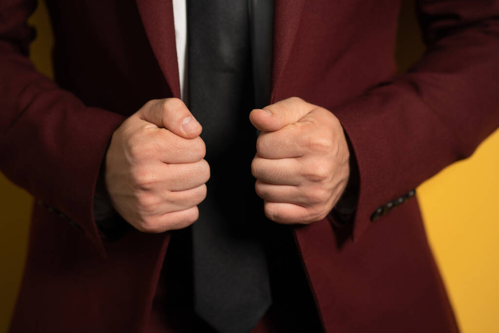 Cerca de las manos sosteniendo un hombre de negocios chaqueta de color burdeos con dos manos fijándola en un cuerpo aislado sobre fondo amarillo - Foto, imagen