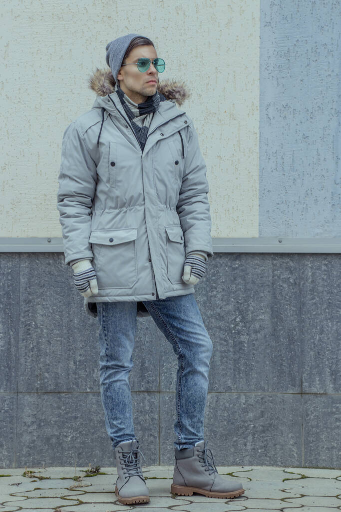 Un homme en vêtements d'hiver se tient sur le fond du mur en pleine croissance et regarde attentivement dans la distance - Photo, image