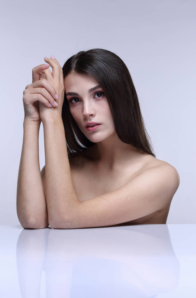 Studio schoonheid portret van een brunette meisje met blote schouders op een lichte achtergrond - Foto, afbeelding