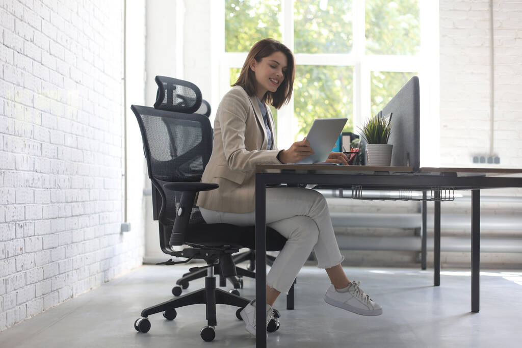 美しい白人ビジネス女性は創造的なオフィスに座っている間、デジタルタブレットを使用して作業しています - 写真・画像