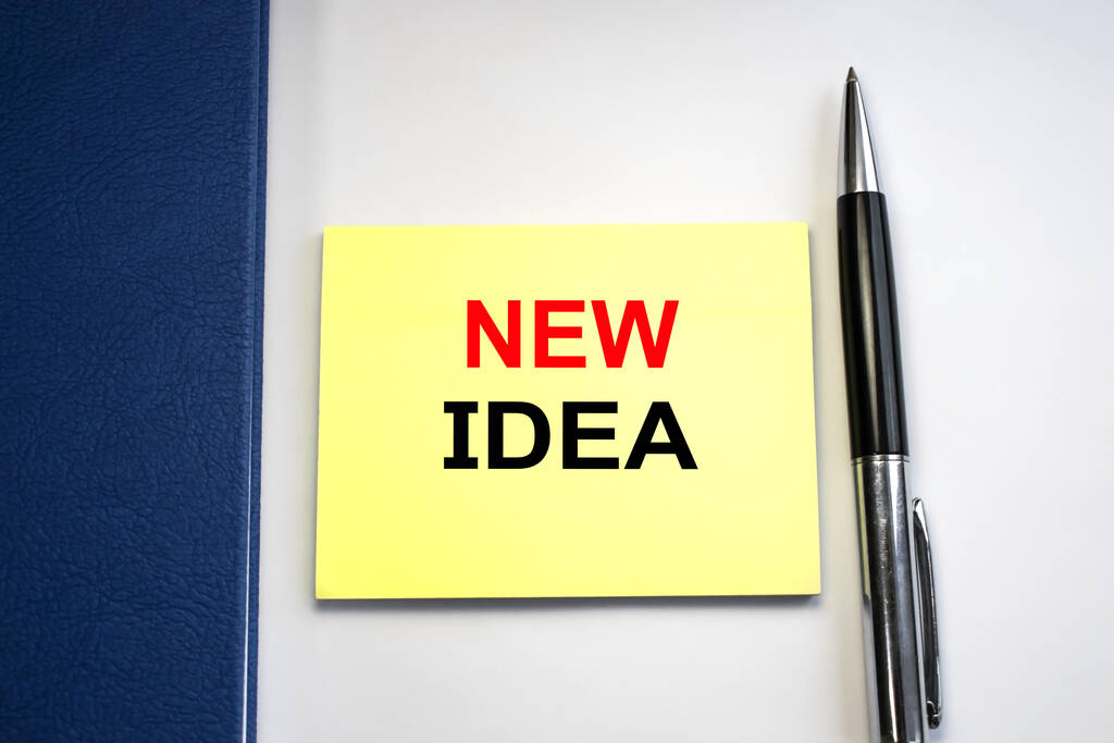 A new idea is written on a piece of paper that is located on a light background among a blue Notepad and pen. - Photo, Image