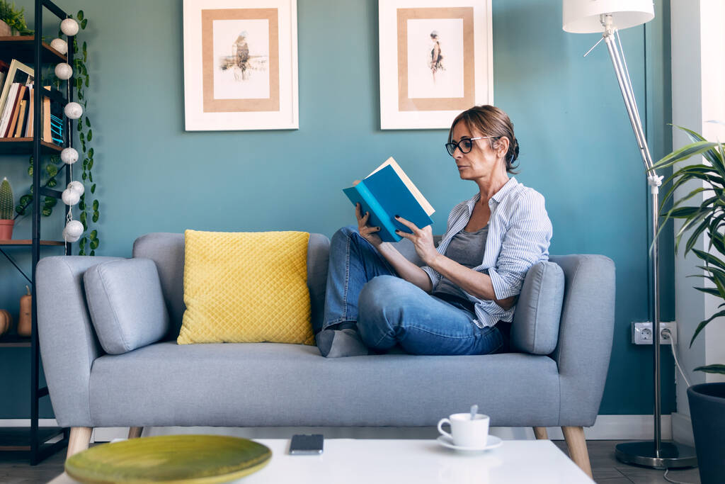 Snímek dospělé krásné ženy čtení knihy sedí na gauči doma. - Fotografie, Obrázek
