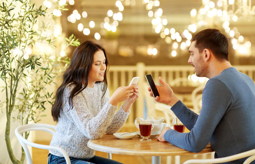 Glückliches Paar mit Smartphones trinkt Tee im Café - Foto, Bild