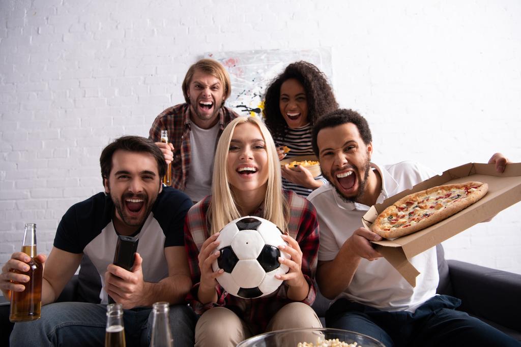 ενθουσιασμένοι πολυεθνικοί φίλοι βλέποντας ποδόσφαιρο πρωτάθλημα με μπύρα και πίτσα, θολό προσκήνιο - Φωτογραφία, εικόνα