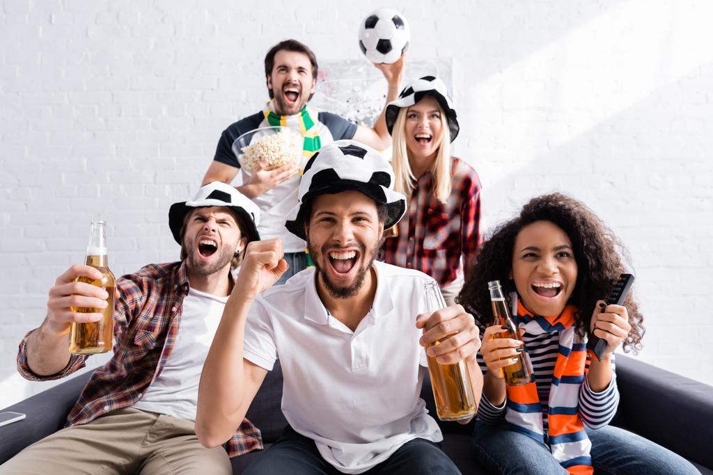 excité amis multiethniques dans les chapeaux de fans de football crier tout en regardant la compétition à la maison - Photo, image