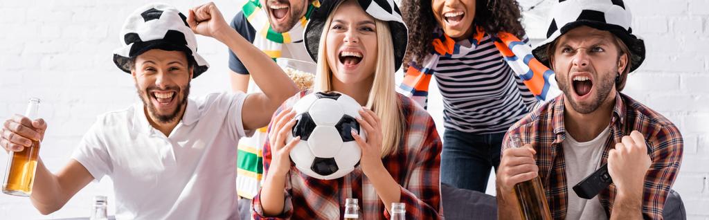 emocionados fanáticos del fútbol multicultural gritando y mostrando el gesto ganador mientras ve el campeonato en casa, pancarta - Foto, Imagen