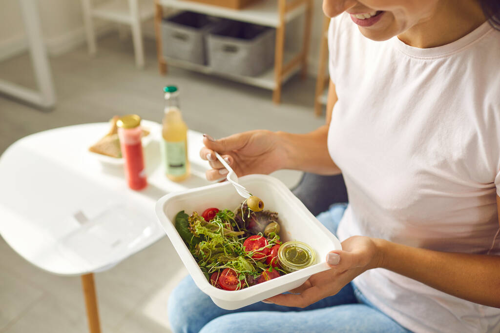 食品配送サービスで配送された容器に健康的なバランスの取れた食事やサラダを食べる笑顔の女性 - 写真・画像