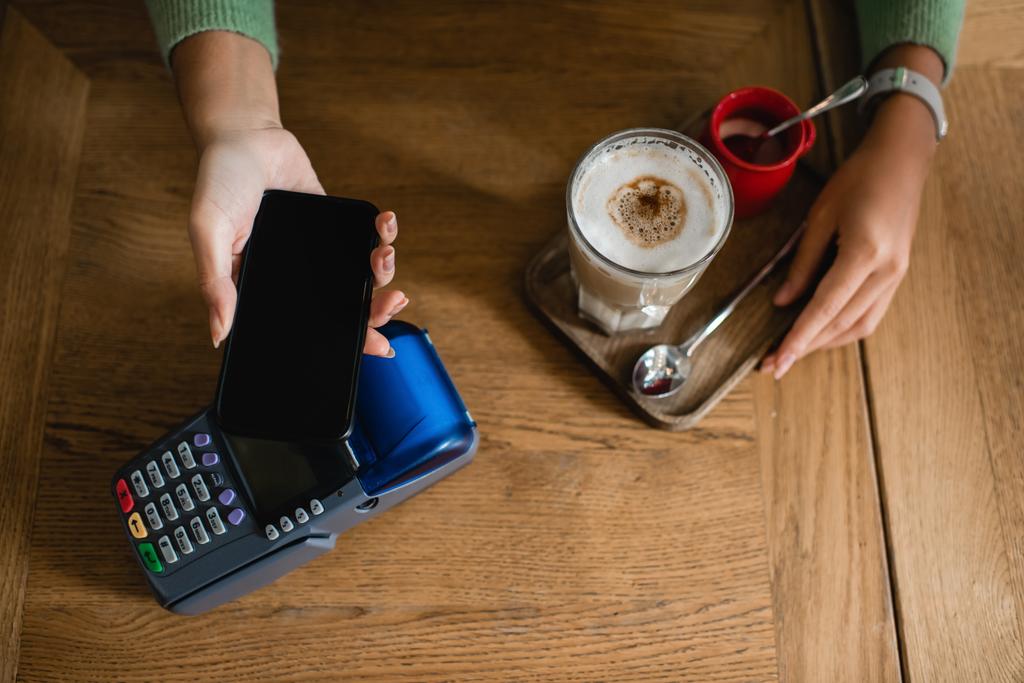 вид зверху на афроамериканську жінку, яка платить за каву зі смартфоном
 - Фото, зображення