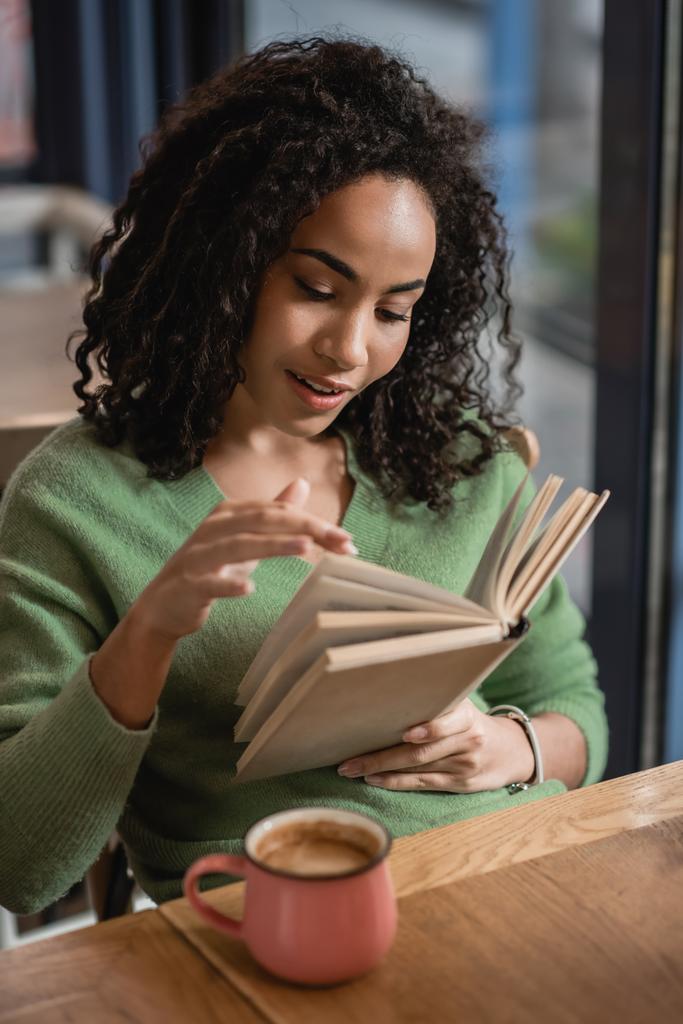 アフリカ系アメリカ人女性がカフェで本のページをめくると - 写真・画像