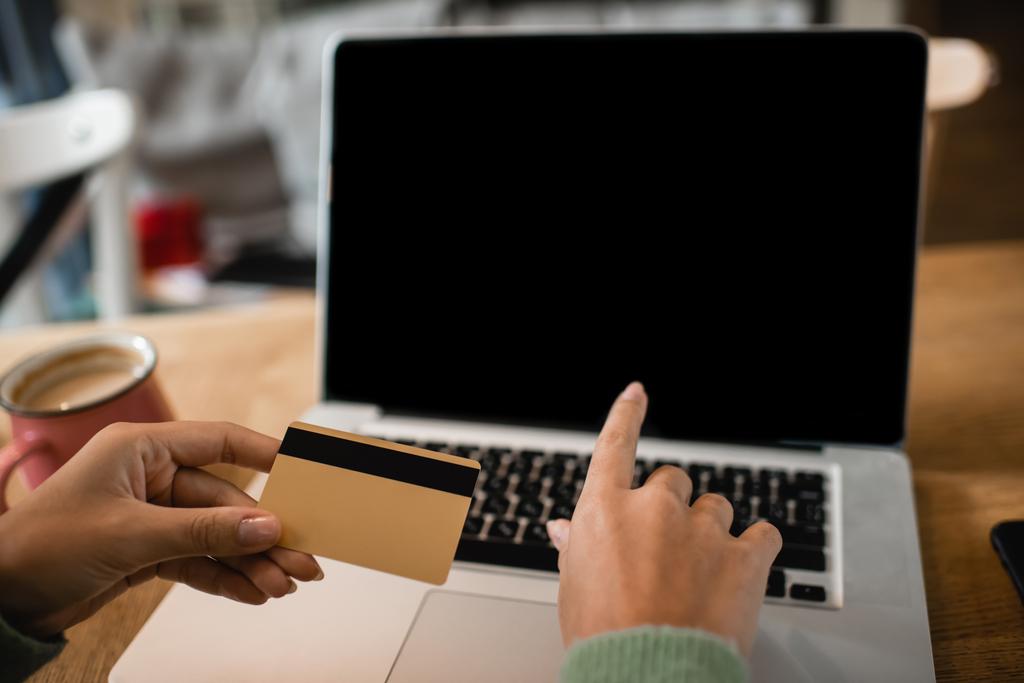 bijgesneden weergave van jong Afrikaans amerikaans vrouw met credit card in de buurt laptop met blanco scherm  - Foto, afbeelding