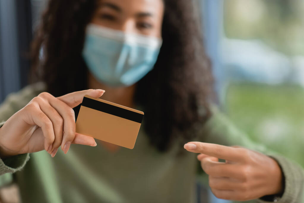 afro-americana em máscara médica apontando com o dedo para o cartão de crédito - Foto, Imagem
