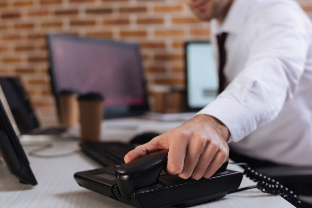 Ausgeschnittene Ansicht eines Geschäftsmannes mit Telefonhörer in der Nähe von Computern auf verschwommenem Hintergrund  - Foto, Bild