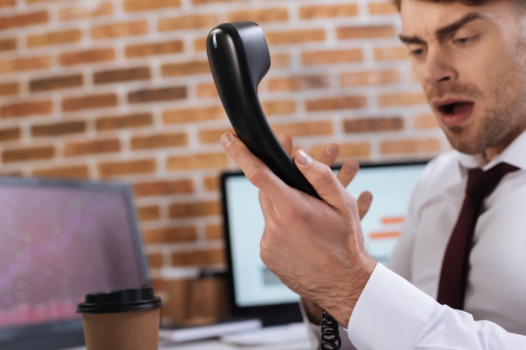 Telefoon headset in de hand van boze zakenman op wazige achtergrond  - Foto, afbeelding