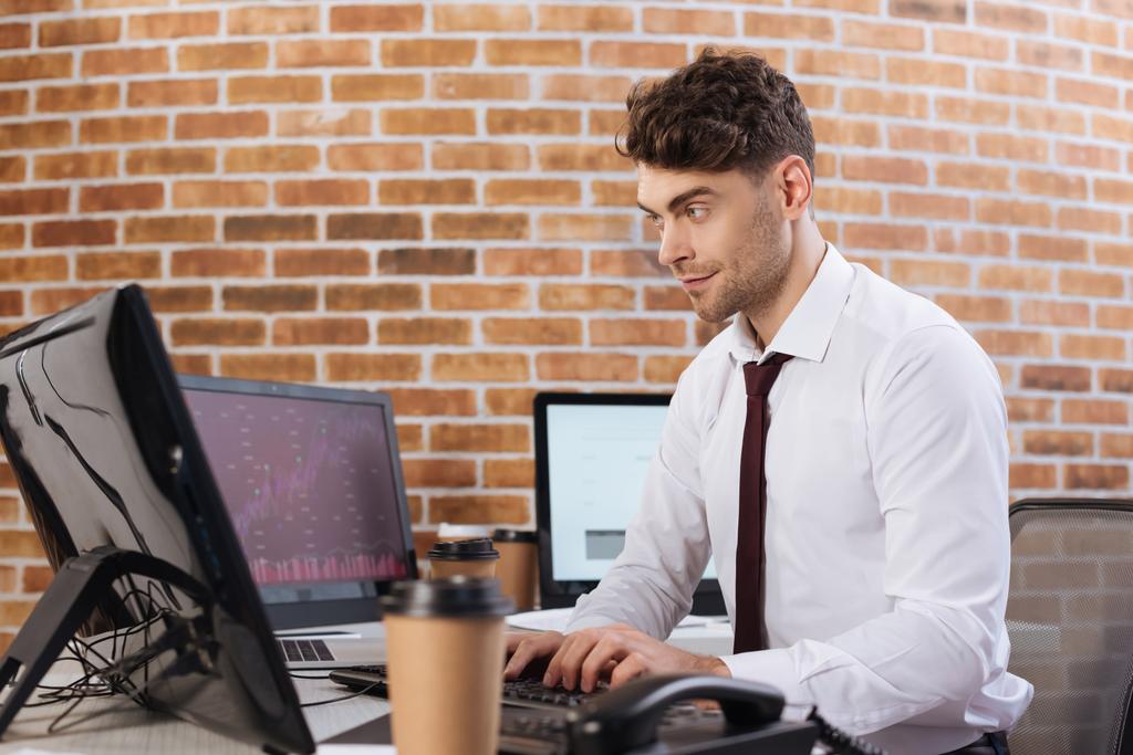 Empresario que usa computadora cerca de monitores con caracteres y café para ir sobre fondo borroso  - Foto, imagen