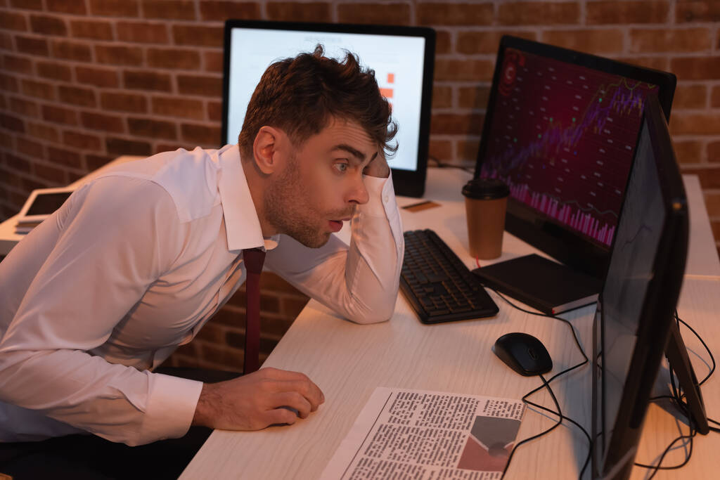 Empresário exausto olhando para monitor de computador perto de jornal no escritório durante a noite  - Foto, Imagem