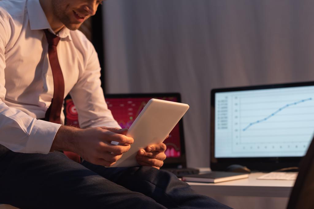 Обрезанный вид цифрового планшета в руках бизнесмена на размытом фоне в офисе вечером  - Фото, изображение
