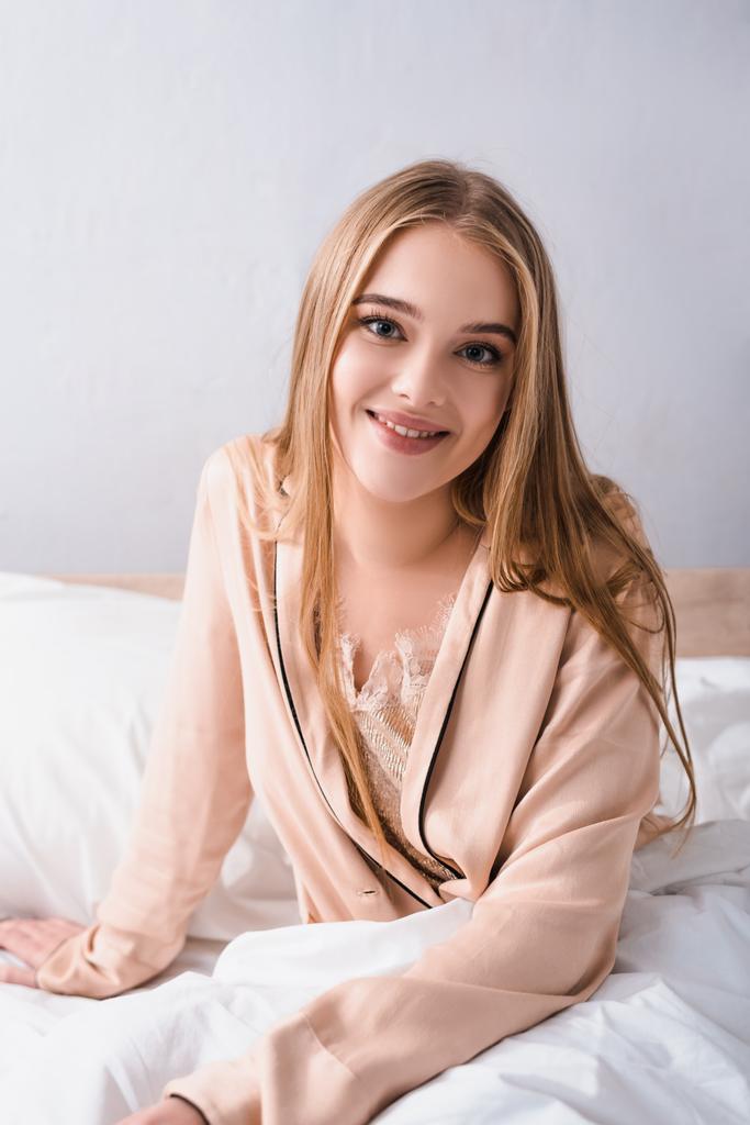 freudige junge Frau in Seidenmantel lächelt im Schlafzimmer  - Foto, Bild